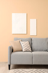Stylish grey sofa with pillows and paintings near beige wall
