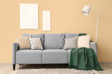 Stylish grey sofa with pillows, blanket and paintings near beige wall