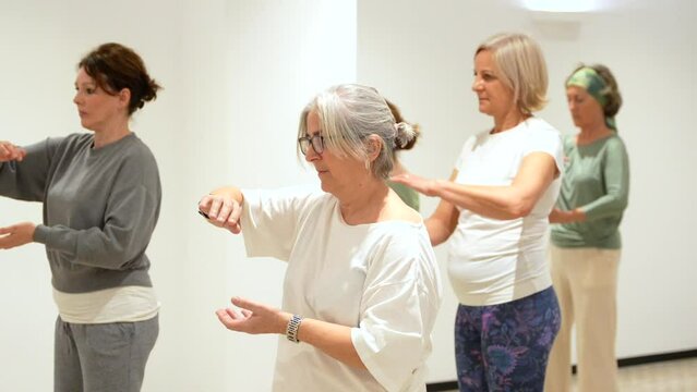 Frontal portrait of a group of caucasian adult concentrated women in a Qi gong classroom