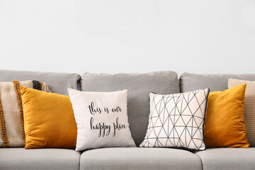 Stylish grey sofa with pillows near white wall