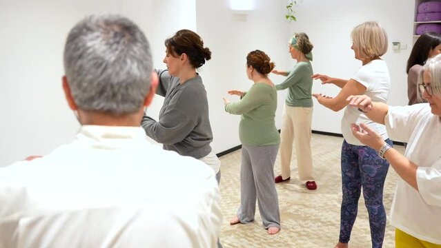 Qi gong male mature teacher leading a class full of mature women in a indoor center