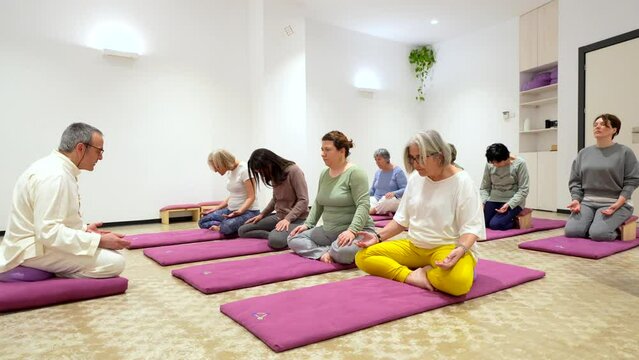 Mature man leading a yoga class full of women doing a lotus position