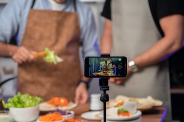 Cropped view of chef influencers presenting fresh salad roll on cooking step by step, streaming via...