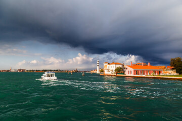 Murano Lighthouse or Faro di Murano is active lighthouse located on Murano island, Venice, Italy, in Venetian Lagoon on Adriatic Sea. View from water bus with dark blue stormy sky in background