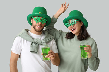 Beautiful young couple in leprechaun hats with glasses of beer on grey background. St. Patrick's...