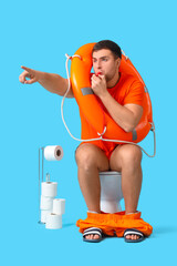 Male lifeguard with ring buoy whistling on toilet bowl against blue background