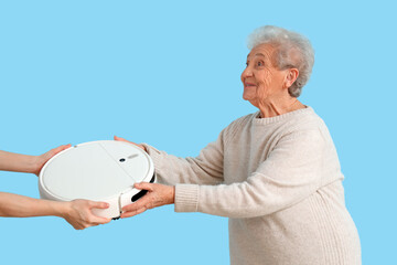 Senior woman receiving robot vacuum cleaner on blue background