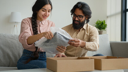 Excited diverse customers couple opening parcel at home happy clients arabian indian woman man unboxing purchase order online shopping store delivery looking inside open box unpacking digital tablet