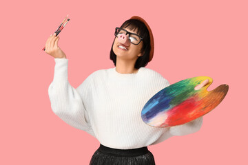 Funny young female artist with palette on pink background. Fool's day