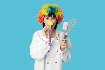 Young laughing female chef with party blower and kitchen utensils on blue background. Fool's day