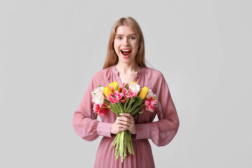 Surprised young woman with bouquet of beautiful tulips on grey background
