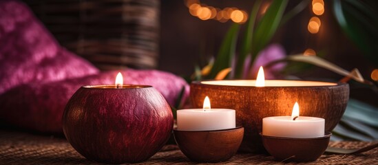 Three burning spa aroma candles, placed on top of a table with a cozy home interior background. The candles are contained in coconut shells and emit a warm, inviting glow.