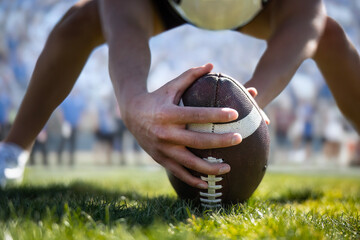 Low-angle close up view of a football player hiking a football during a football game. Focus on the ball and hands. Selective focus image. Unique view. 