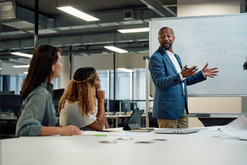 Four multiracial business people in businesswear talking and gesturing during meeting in office