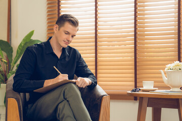 Portrait of happy and smiling male psychologist portrait sitting on arm chair in psychiatrist office or therapy room. Friendly and professional mental healthcare counselor and therapist. Unveiling