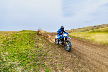 Person motorcycling on dirt road with sky and grass in background