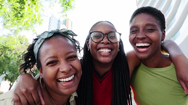 Three laughing and joyful young African American women embracing and looking at camera outdoors. Group black nice females friends having fun together sunny day. Generation z and positive relationships