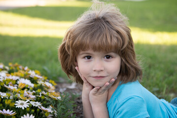 Charming blond child on background of flowers in summer. Pretty little child working in garden, child taking care of flowers, enjoying warm and sunny day.