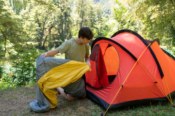 A young man arranges his camping tent and sleeping bag at the campsite during his summer walk...