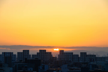 都市の夜明け。神戸市から芦屋大阪方面をのぞむ。生駒の山並みから朝日が昇る。都市のビルがシルエットで浮かぶ。