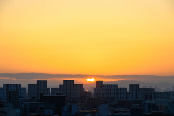 Fototapeta premium 都市の夜明け。神戸市から芦屋大阪方面をのぞむ。生駒の山並みから朝日が昇る。都市のビルがシルエットで浮かぶ。