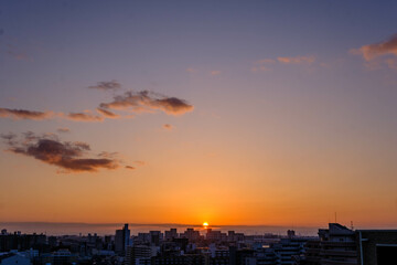 都市の夜明け。神戸市から芦屋大阪方面をのぞむ。生駒の山並みから朝日が昇る。都市のビルがシルエットで浮かぶ。