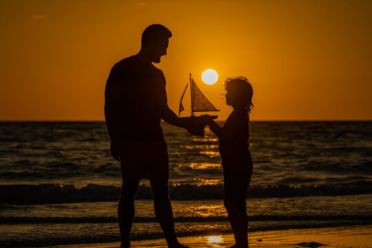 Father and son kid playing with toy boat, toy ship. Travel and adventure concept. Father and son feeling adventurous while cruising. Father and son on summer sunset beach. Fathers day.