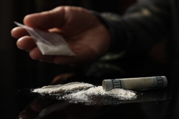 Drug addiction. Man with cocaine and rolled dollar banknote at black table, selective focus - obrazy, fototapety, plakaty