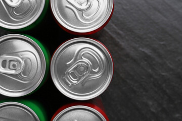 Energy drink in cans on black textured background, top view. Space for text