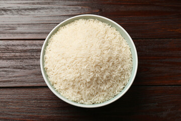 Raw basmati rice in bowl on wooden table, top view