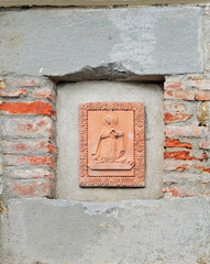 Very old terracotta bas-relief picturing a woman and a dog on a street wall in Cortona, Tuscany, Italy