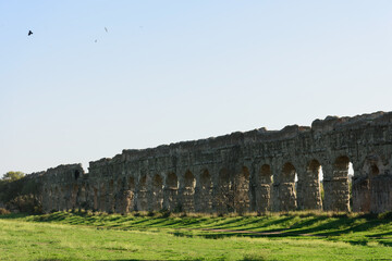 The long arched wall of an ancient Roman aqueduct along a walking path in a park, evening shadows from the setting sun shadows fall on the ground in a beautiful pattern