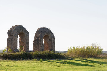 Remains of ancient stone ruins of a Roman aqueduct, vertical stone arches on an empty green meadow in a park