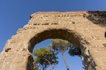 Through the arched opening of the ancient stone Roman aqueduct in the park you can see tall slender...