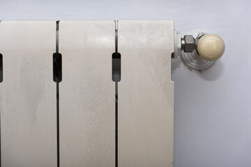 A white heating radiator hangs on a white wall in a room, heat is regulated