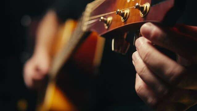 Young musican man checking strings of acoustic guitar close-up. Male guitarist tuning sound of musical instrument. 