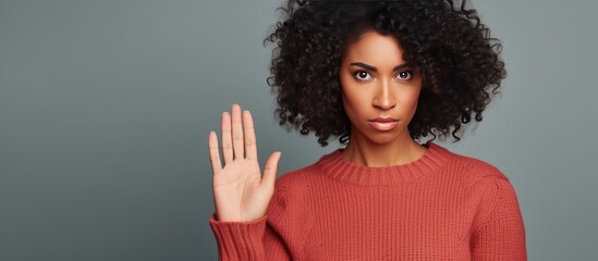 A beautiful African American woman wearing a red sweater is holding her hand up in a stop sign gesture. She has a negative and serious expression on her face.