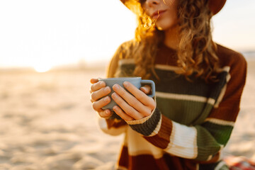 Young woman drinking morning coffee on the beach. Cup of coffee to keep warm. Travel, weekend,...