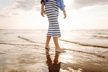 Close- up leg of young woman walking along wave of sea water and sand on the summer beach. Travel, weekend, relax and lifestyle concept.