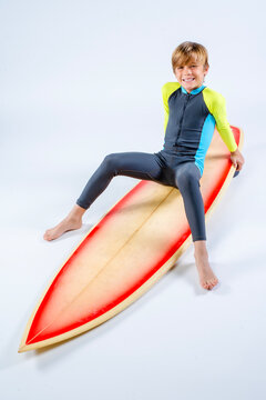 Young surfer boy smiling happy sitting straddling his surfboard