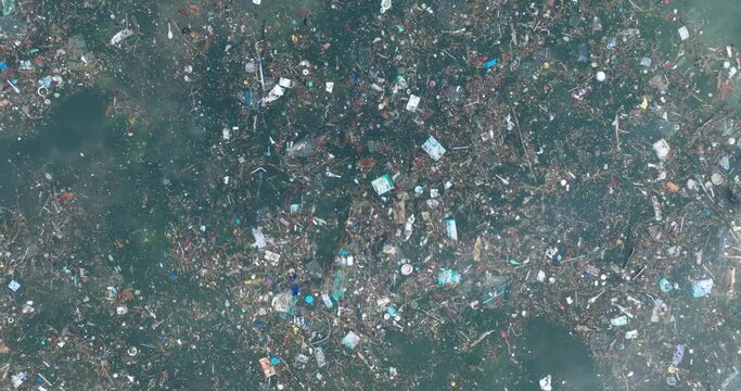 Low altitude top down drone shot of polluted water filled with trash floating over dead coral reef in the turqouise tropical water of Bali Indonesia
