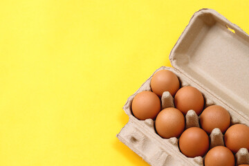 Chicken eggs in a cardboard box ready to cook on a yellow background