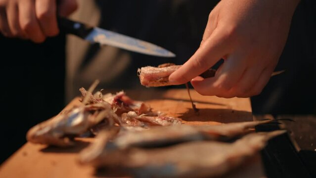 Close-up. A man cleans salty dried cured fish with his hands on a wooden board and then helps peel it with a kitchen knife