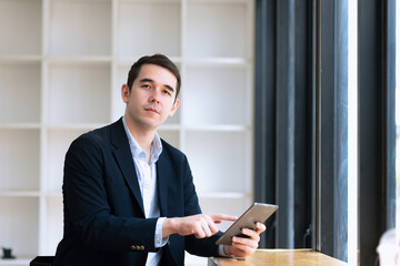 Businessman using tablet sitting at desk in office.