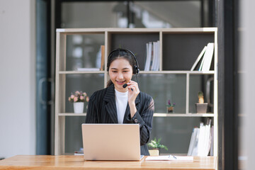 Asian businesswoman using laptop with earphones and working at desk in the office.