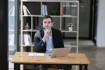 Businessman using laptop with earphones and working at desk in the office.