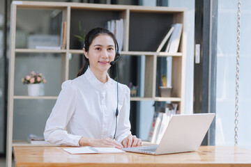 Asian businesswoman using laptop with earphones and working at desk in the office.