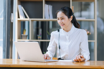 Asian businesswoman using laptop with earphones and working at desk in the office.