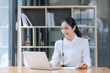 Asian businesswoman using laptop with earphones and working at desk in the office.