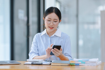 Asian accounting woman using smartphone working with document paper and laptop computer at table office, Financial and accounting woman concept. 
